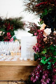 wine glasses are lined up on a table with flowers and greenery in the background