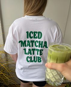 a woman holding a drink in her right hand and wearing a white t - shirt that says iced matcha latte club