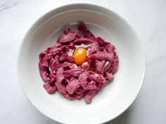 a white bowl filled with meat and an egg