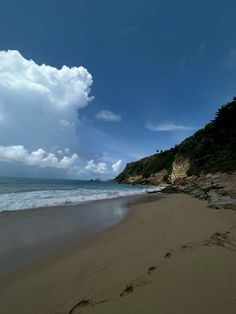 a sandy beach next to the ocean under a cloudy blue sky