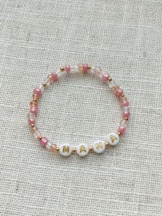 Mommy and Littles Co pink mama bracelet. Details: *4mm seed beads. *acrylic gold and white letter beads. *3 mm 14k gold plated beads. *Made with jewelry quality elastic. *please message if you are needing a size that is not listed! *NOTE: this listing is for ONE bracelet. Mama Bracelet Beads, Handmade White Friendship Bracelets For Mother's Day, Handmade White Beaded Bracelets For Mother's Day, White Hypoallergenic Dainty Name Bracelet, Beaded Heishi Beads Name Bracelet For Gift, White Round Beads Friendship Bracelets For Mother's Day, Beaded Heishi Name Bracelet As Gift, Custom Name Heishi Beads Bracelet As Gift, Trendy White Name Bracelet For Mother's Day