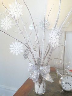 a vase filled with branches and snowflakes on top of a table next to an alarm clock