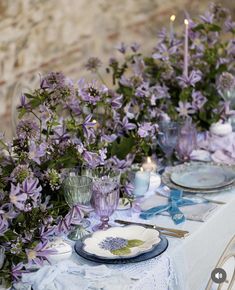 the table is set with purple flowers and blue china plates, candles and napkins