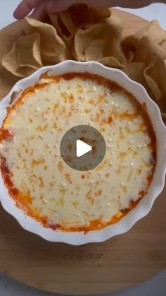 a white bowl filled with cheese on top of a wooden cutting board next to tortilla chips