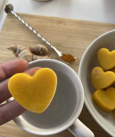 a person holding a heart shaped cookie in front of two white bowls filled with yellow hearts