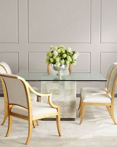 a glass table with chairs around it in front of a gray wall and white carpet