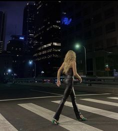 a woman walking across a cross walk at night