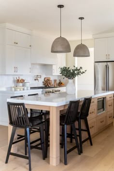 a kitchen with two black chairs sitting at the center of the table and three pendant lights hanging from the ceiling