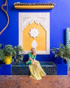 a woman sitting on a bench in front of a blue and yellow wall with potted plants