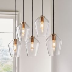 four clear glass pendant lights hanging from a ceiling fixture in a room with white walls and windows