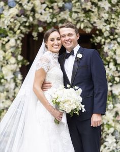 a bride and groom pose for a photo in front of a flower covered archway at their wedding