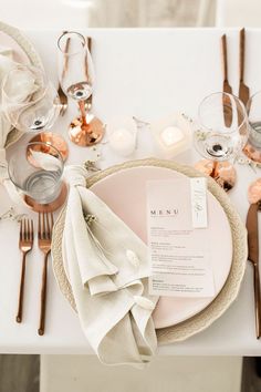 a place setting with silverware, napkins and candles on a white table cloth