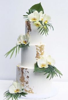 a three tiered cake with white flowers and greenery on it's side