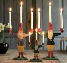 three gnome figurines holding lit candles in their hands