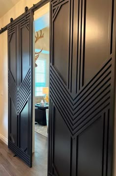 two black doors are opened to reveal a living room with wood floors and white walls