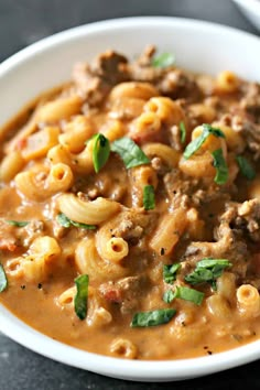 a white bowl filled with pasta and meat in gravy on top of a table