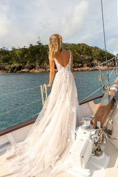 a woman in a wedding dress standing on the deck of a boat looking out over the water