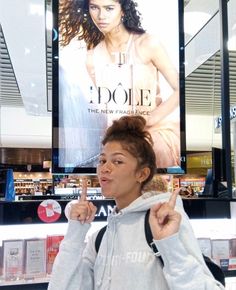 a woman pointing to the side in front of a magazine cover with an advertisement behind her