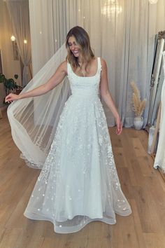 a woman in a white wedding dress standing on a wooden floor with her arms out