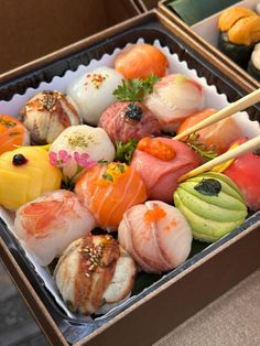 an assortment of sushi in a box with chopsticks