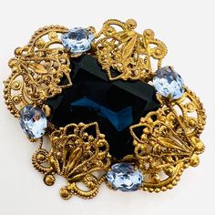 Beautiful Vintage WEST GERMANY Sapphire Blue Glass & Rhinestone Brooch. Ornate gilt filigree metal set with large center sapphire blue glass and accented with light blue rhinestones. Not signed but is known West Germany. In excellent vintage condition with minimal age appropriate wear. Measures 2 inches long by 1 7/8 inches wide. Roll over clasp secure. Elegant Blue Gemstone Brooch, Elegant Blue Gemstone Brooches, Blue Art Deco Formal Brooch, Antique Blue Jewelry With Brooch, Victorian Blue Brooch For Formal Occasions, Blue Victorian Brooch For Formal Occasions, Formal Blue Gemstone Brooch, Blue Victorian Brooches For Formal Occasions, Art Deco Blue Brooches As Gifts