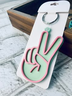 a pink and green peace sign keychain hanging from a white tag on a table