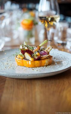 a white plate topped with food on top of a wooden table next to wine glasses