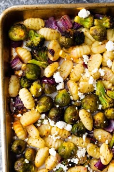 a casserole dish with brussel sprouts, broccoli and red onions