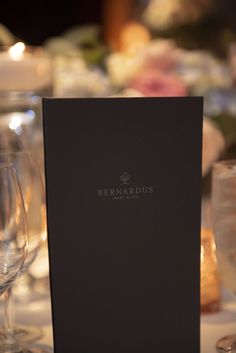 an empty menu sitting on top of a table with wine glasses and candles in the background