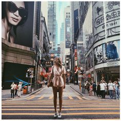 a woman standing in the middle of a crosswalk on a busy city street with tall buildings