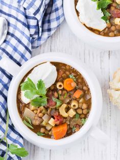 two white bowls filled with beans, carrots and sour cream on top of a wooden table