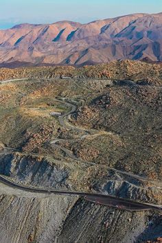 an aerial view of a winding road in the desert with mountains in the back ground