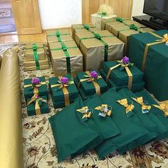 many presents are wrapped in green paper and tied with gold ribbon, sitting on the floor