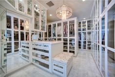 a walk in closet with lots of white drawers and glass doors on the walls, along with a chandelier hanging from the ceiling