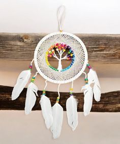 a white dream catcher hanging from a wooden beam with colorful beads and a tree on it