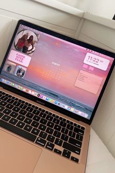 an open laptop computer sitting on top of a white couch next to a window with pink and black accents