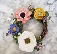 a wreath made out of felt flowers on a marble counter top with greenery around it