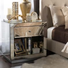 a mirrored nightstand with pictures and candles on it next to a white rug in front of a bed