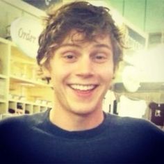 a man with curly hair smiling at the camera in a store or office building,