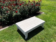 a wooden bench sitting on top of a lush green field next to a bush filled with red flowers