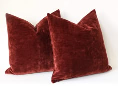 two red velvet pillows sitting side by side on a white surface, one is turned down