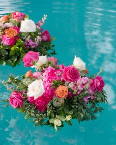 two vases filled with flowers sitting on top of a blue pool next to each other