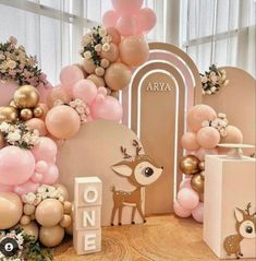 a table topped with balloons and deer figurines next to a wall covered in pink, gold and white balloons