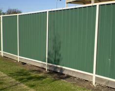 a large green fence is in front of a building and some grass on the ground