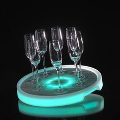 five wine glasses sitting on top of a tray with green light in the dark background