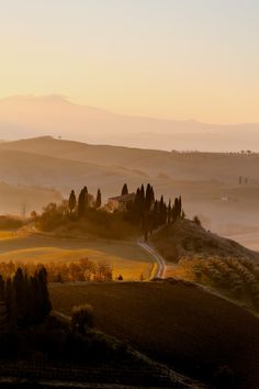 the sun is setting over a rural landscape with rolling hills and trees in the foreground