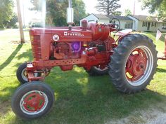 an old red farmall tractor parked in the grass