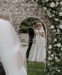 a bride and groom standing in front of a mirror with the reflection of their wedding day