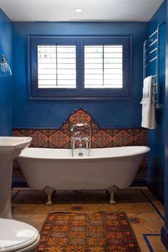 a bathroom with blue walls and a white bathtub next to a toilet under a window