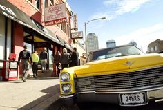 an old yellow car is parked on the side of the road in front of a store